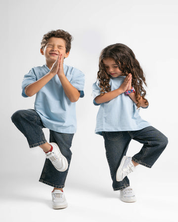 Two children wearing matching light blue shirts and dark jeans on a white background