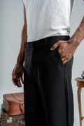 Person wearing black pants with a white shirt, standing next to a suitcase.