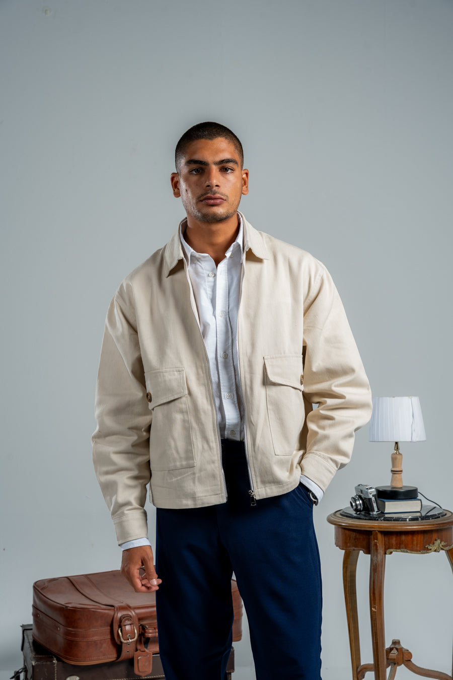 Man wearing a beige jacket over a white shirt with a gray background