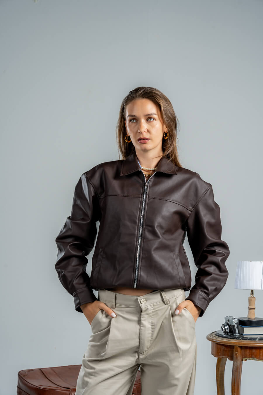 Woman wearing a brown leather jacket and beige pants against a plain background