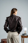 Person wearing a dark leather jacket and beige pants against a plain background
