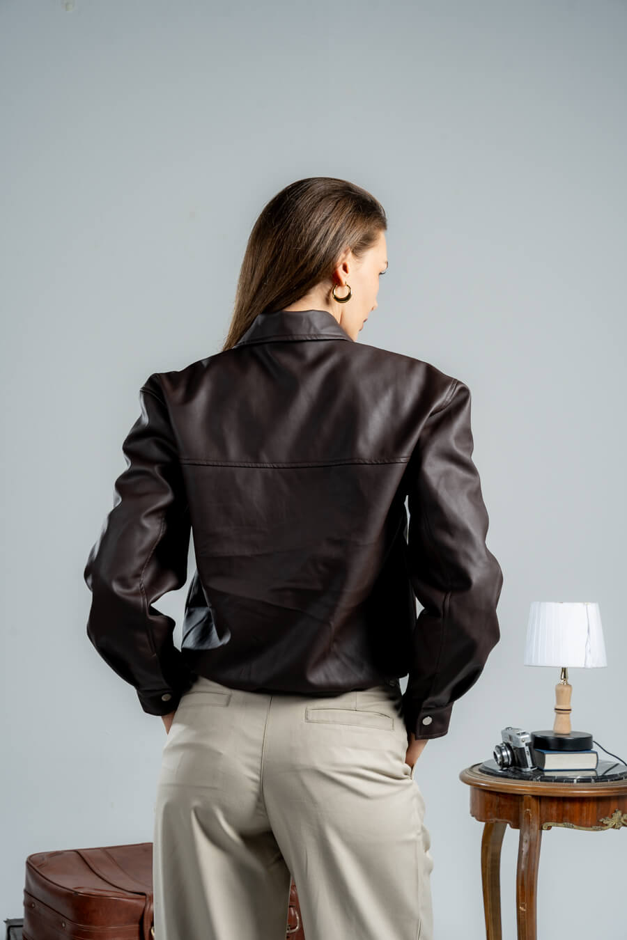 Person wearing a dark leather jacket and beige pants against a plain background