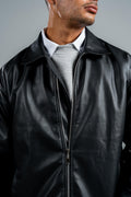 Man wearing a black leather jacket over a gray sweater on a gray background