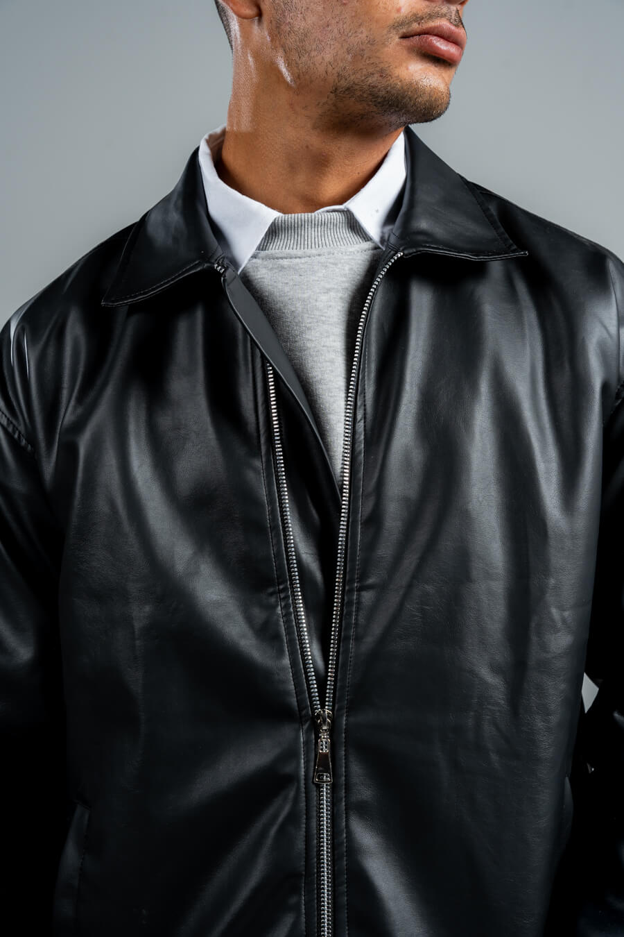 Man wearing a black leather jacket over a gray sweater on a gray background