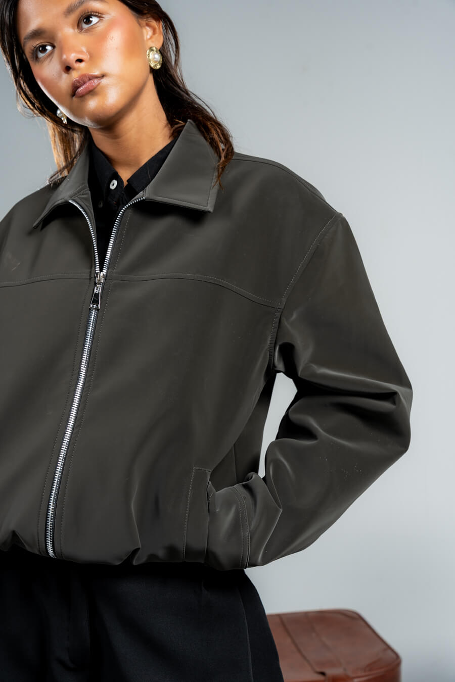 Woman wearing a dark green jacket and black pants against a plain background