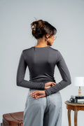 Woman wearing a gray long-sleeve top and gray pants against a plain background