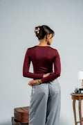 Person wearing a burgundy long-sleeve top and gray pants against a plain background