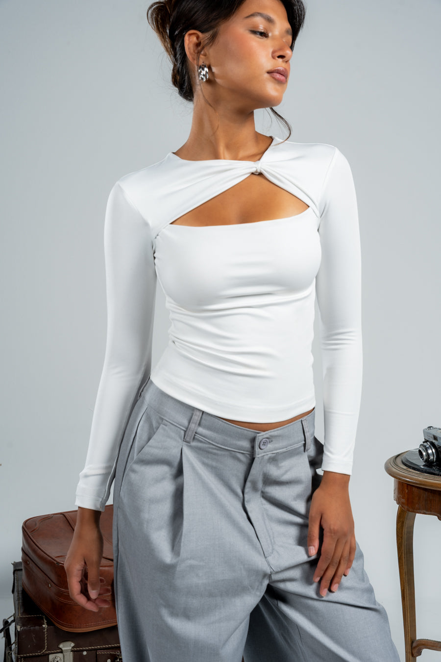 Woman wearing a white long-sleeve top with cut-out design and gray pants against a plain background