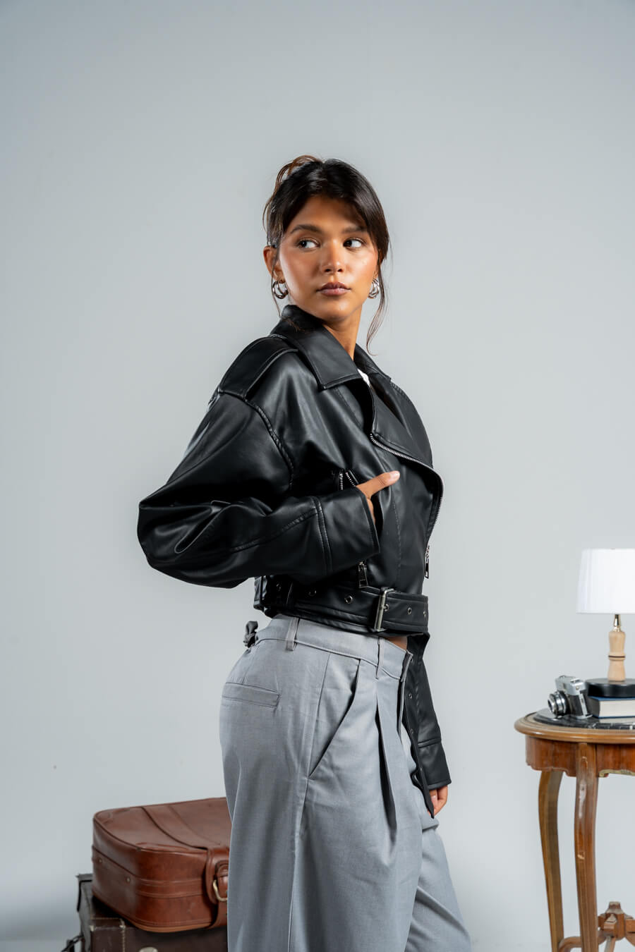 Woman wearing a black leather jacket and gray pants against a plain background