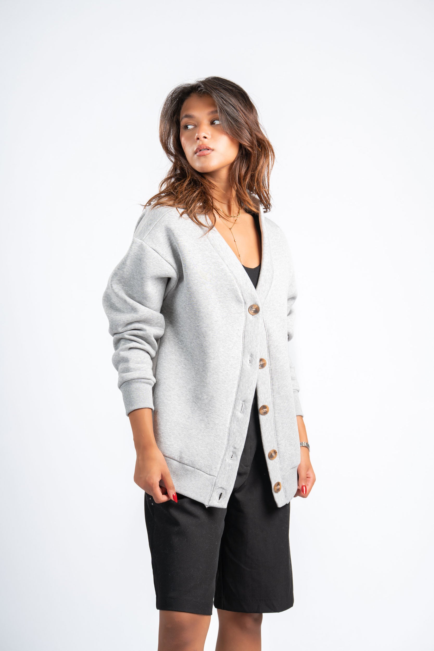 Woman wearing a light gray cardigan over a black top and shorts on a white background