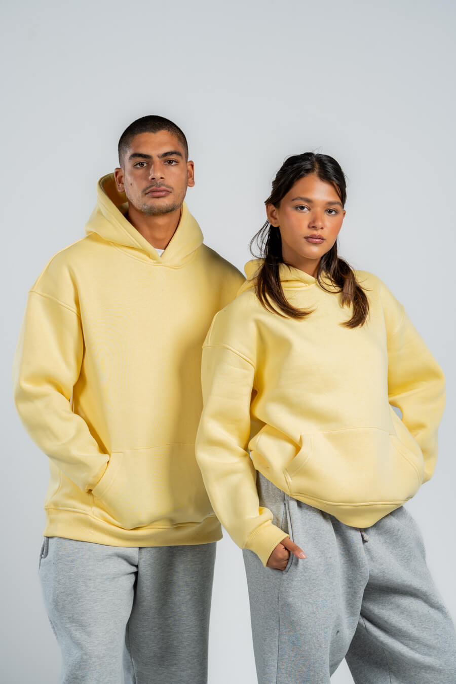 Two people wearing matching yellow hoodies and gray pants against a plain background