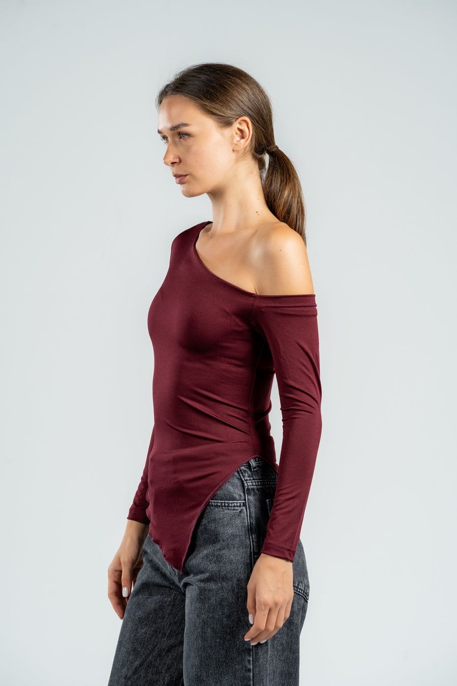 Woman wearing a burgundy off-shoulder top and gray jeans on a light gray background