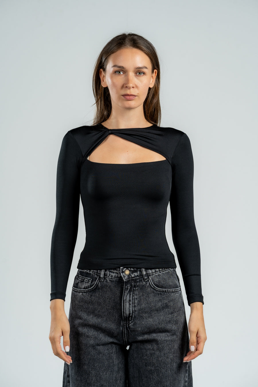 Woman wearing a black long-sleeve top with a unique design, standing against a plain background.