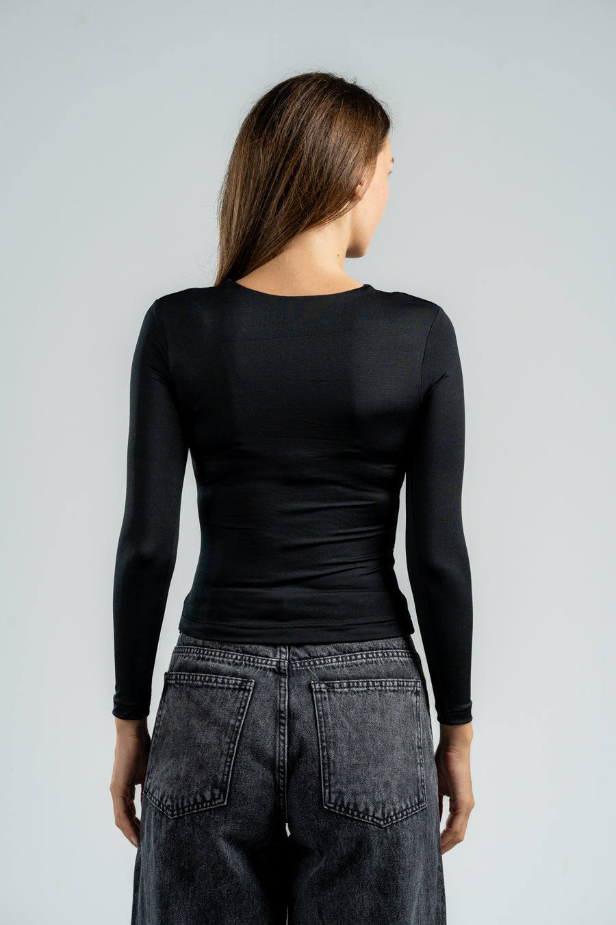 Person wearing a black long-sleeve top and gray jeans on a light gray background