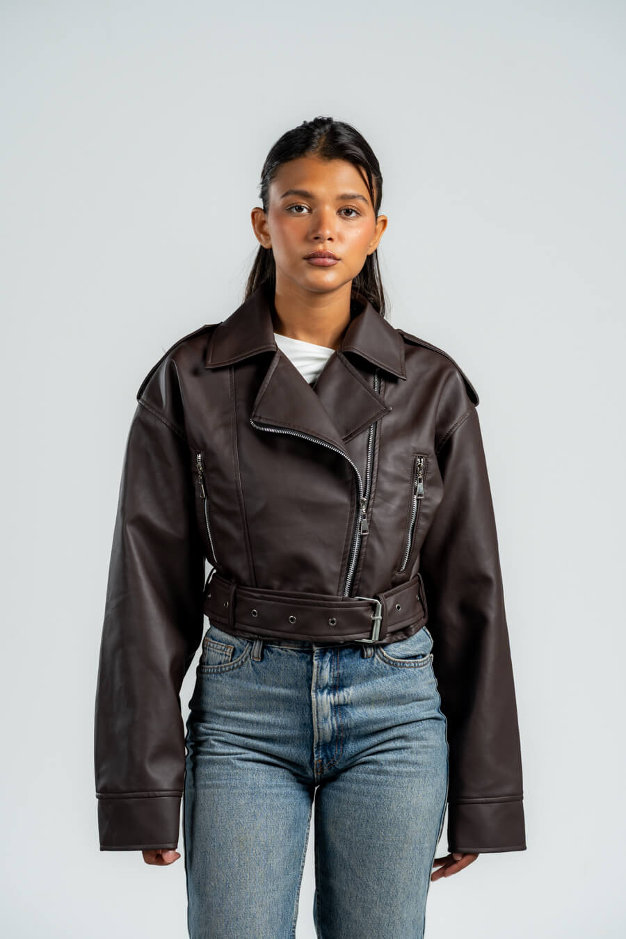 Person wearing a brown leather jacket and blue jeans against a white background