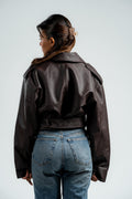 Person wearing a brown leather jacket and blue jeans on a plain background