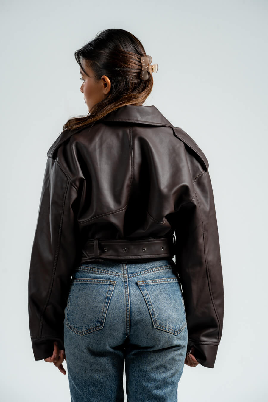 Person wearing a brown leather jacket and blue jeans on a plain background