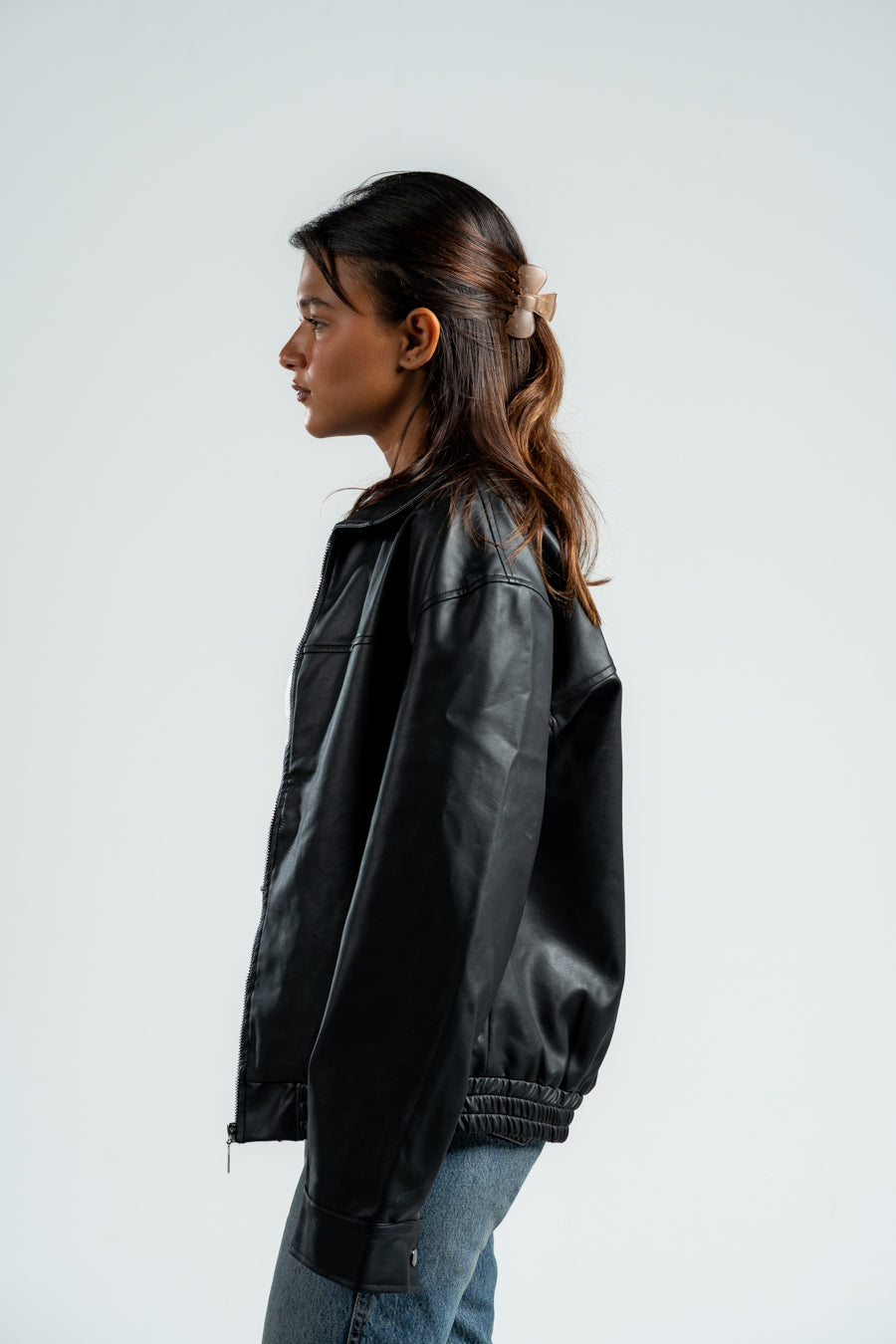 Person wearing a black leather jacket and blue jeans on a white background