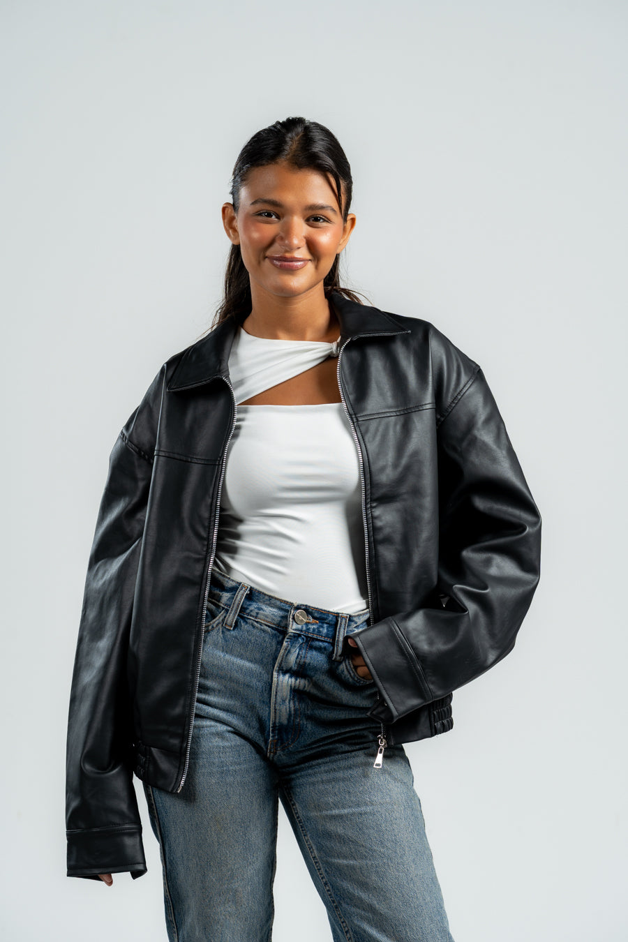 Person wearing a black leather jacket and blue jeans on a white background
