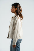 Woman wearing a beige jacket and blue jeans against a white background