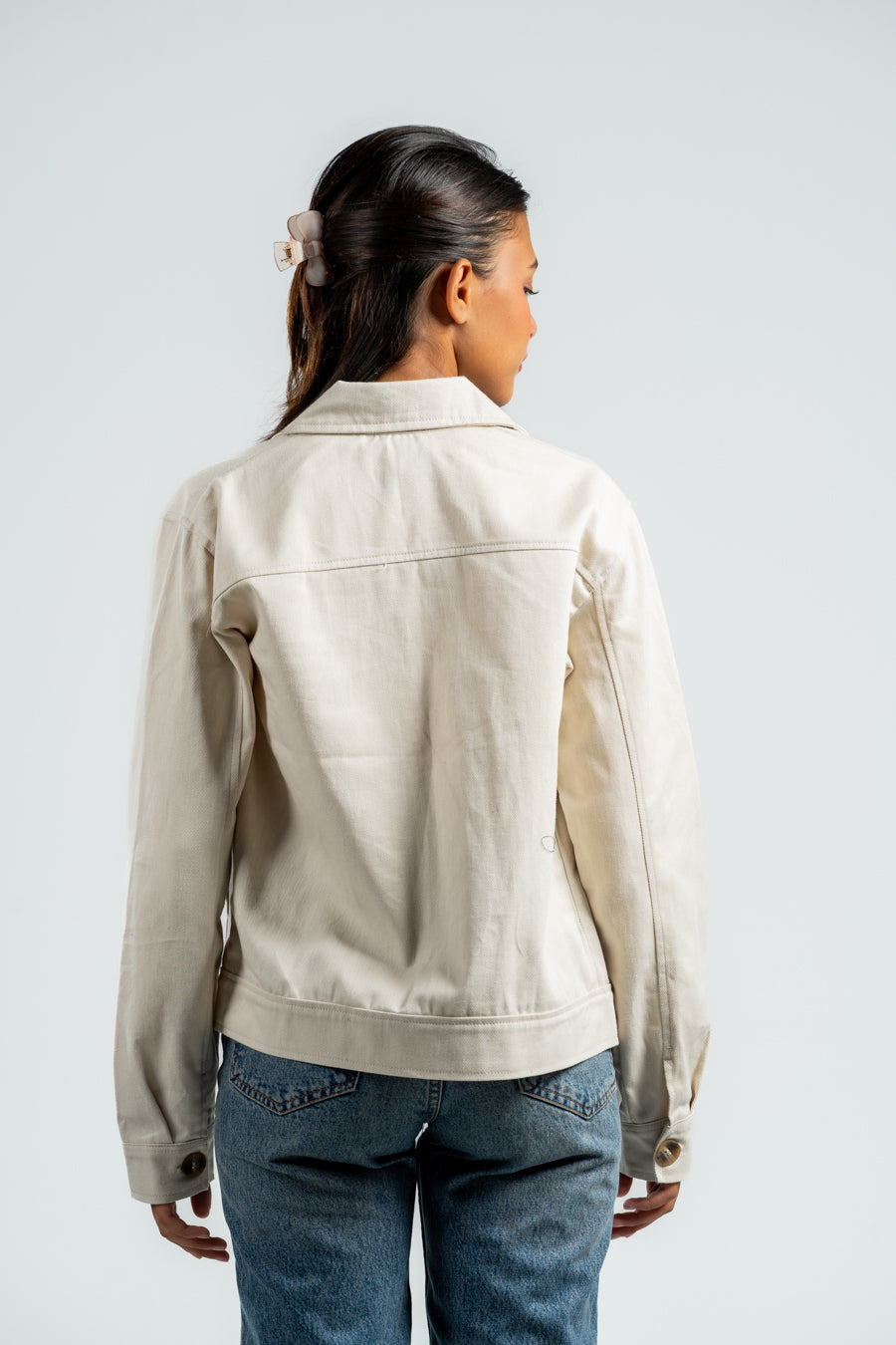 Person wearing a beige jacket and blue jeans on a plain background