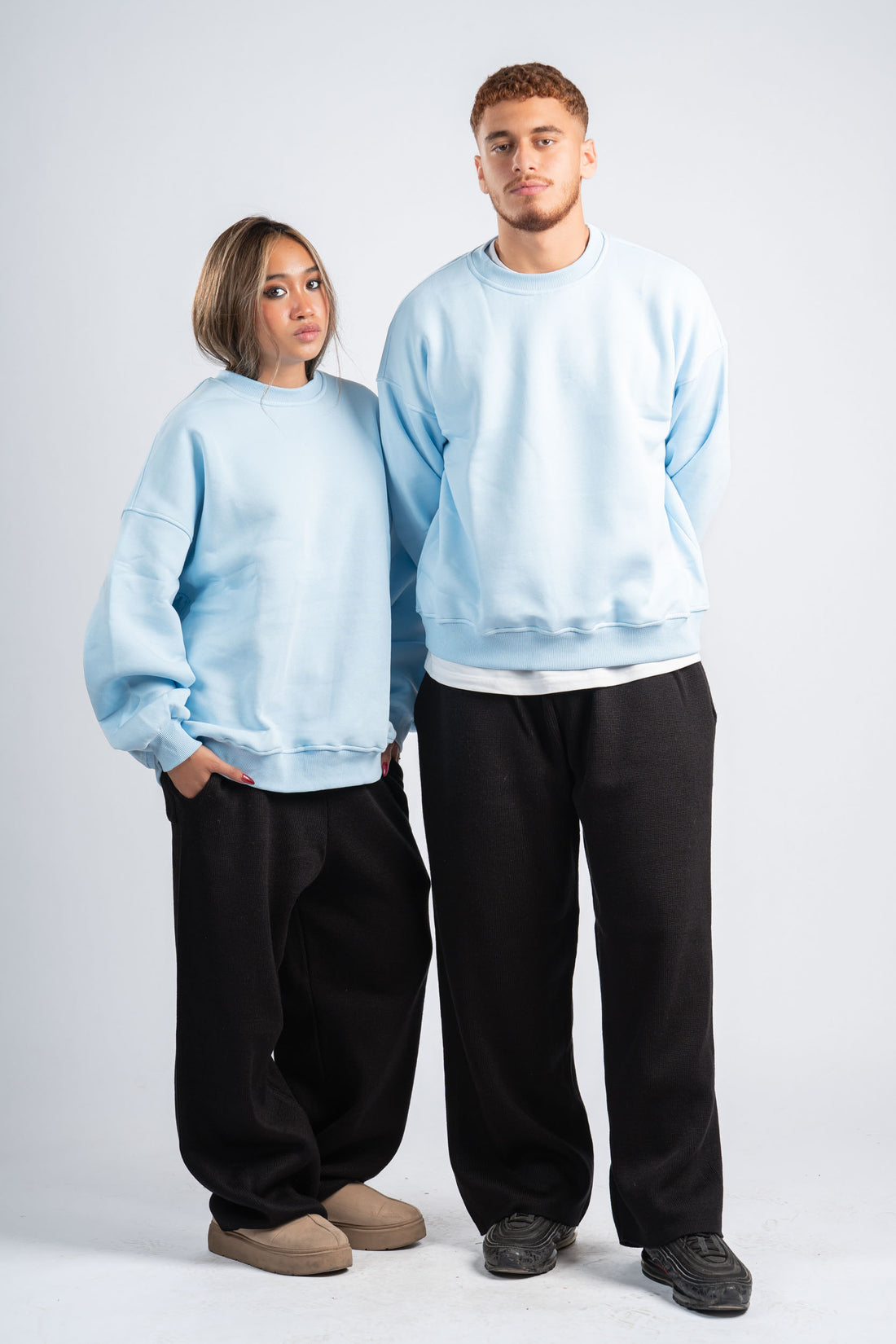 Two people wearing matching light blue sweatshirts and black pants on a white background