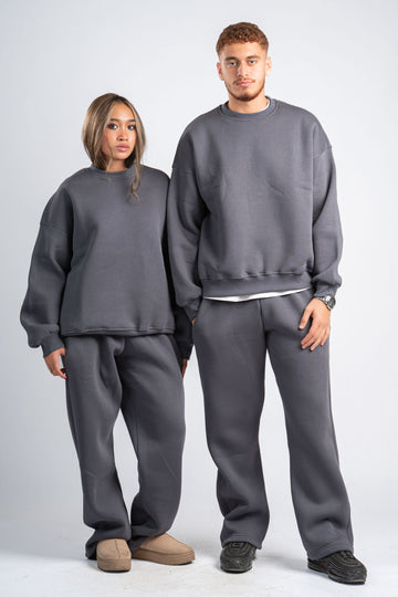 Two people wearing matching gray sweatshirt and pants sets on a plain background
