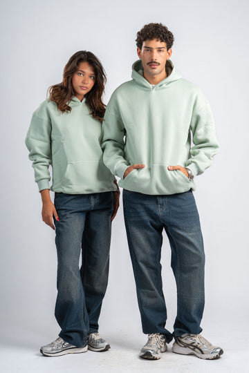 Two people wearing light green hoodies and dark jeans on a white background