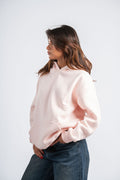 Woman wearing a light pink hoodie and blue jeans on a white background