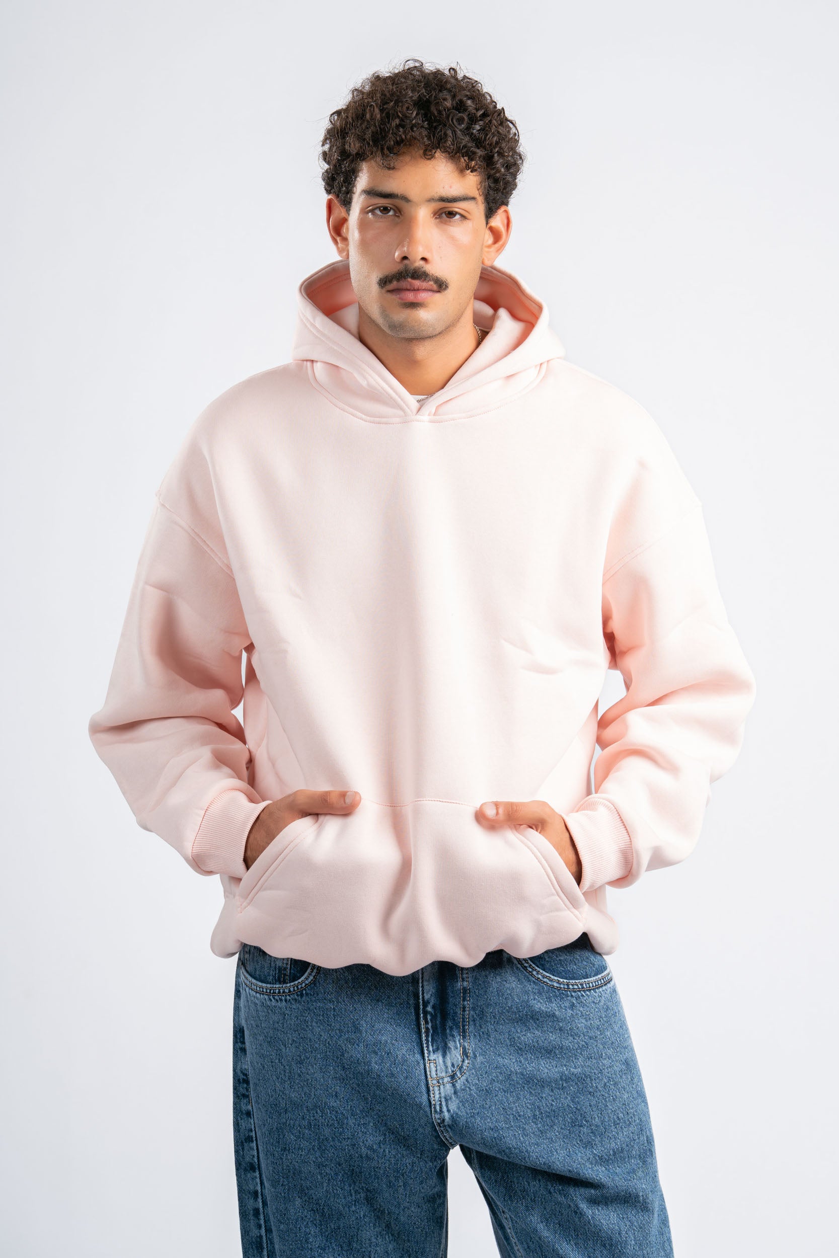 Man wearing a light pink hoodie and blue jeans on a white background