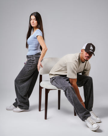 Two people wearing oversized jeans and casual clothing on a plain background