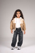 Child wearing a beige jacket, white shirt, and dark jeans on a plain background