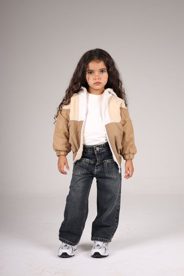 Child wearing a beige jacket, white shirt, and dark jeans on a plain background