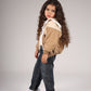 Young girl wearing a beige jacket, white shirt, blue jeans, and white sneakers on a plain background