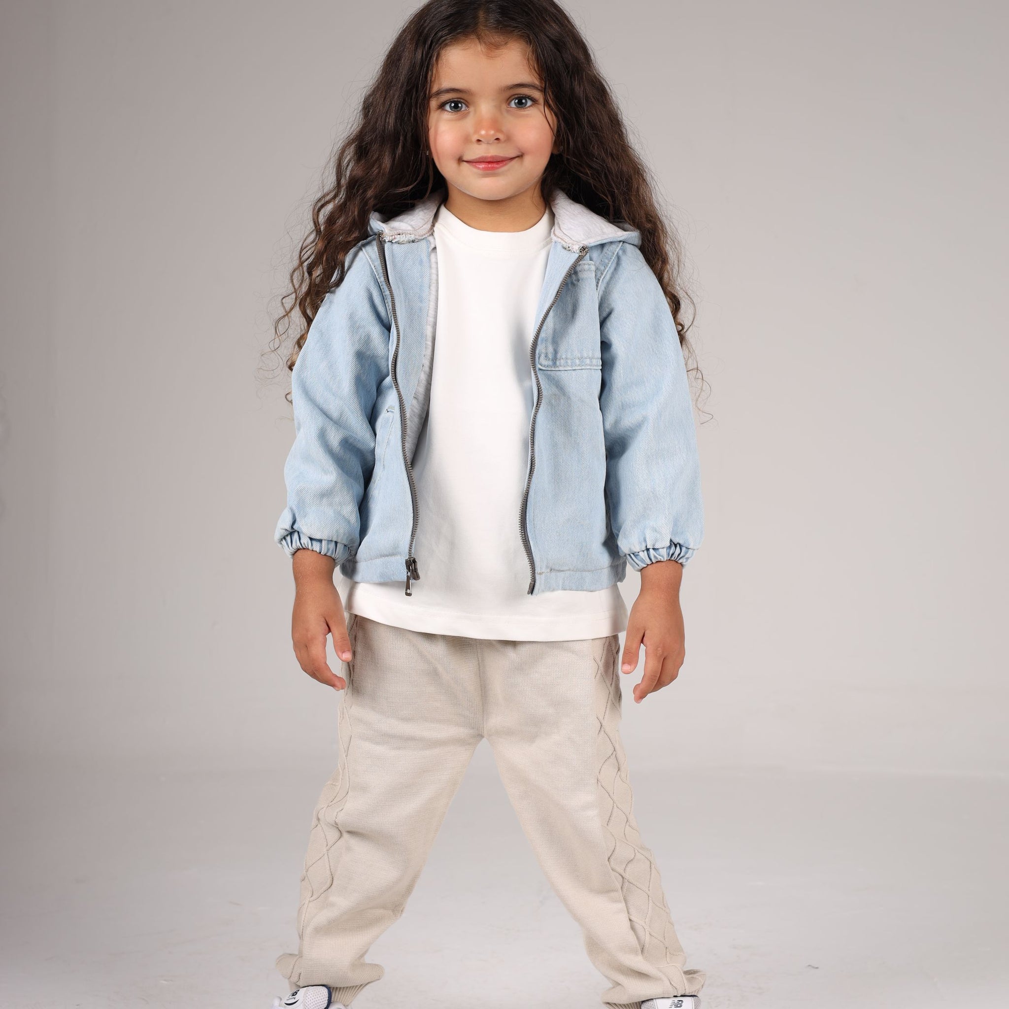 Child wearing a light blue denim jacket, white shirt, beige pants, and sneakers on a gray background