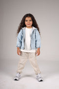 Child wearing a light blue denim jacket, white shirt, beige pants, and sneakers on a gray background