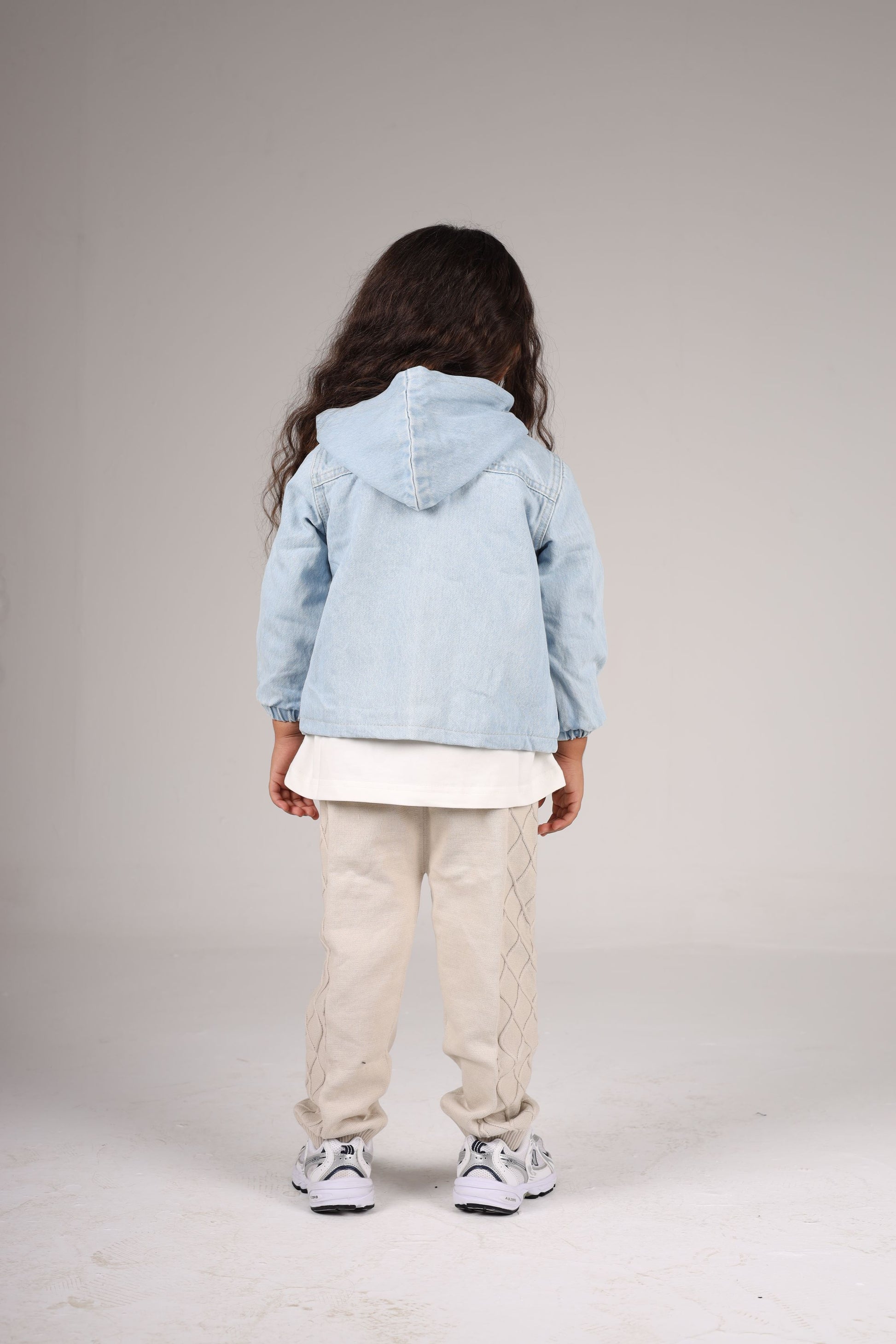 Child wearing a light blue denim jacket on a plain background