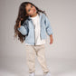 Child wearing a denim jacket, white shirt, beige pants, and sneakers on a plain background