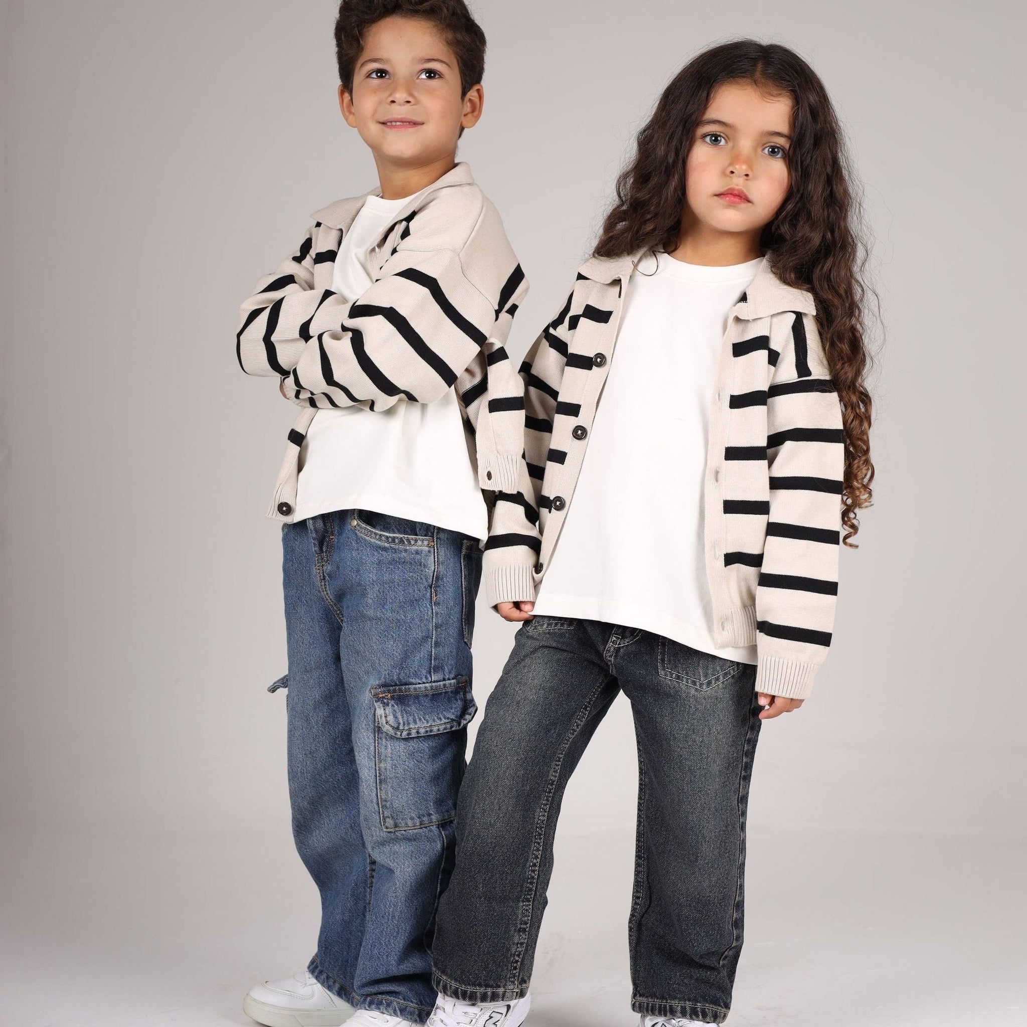 Two children wearing matching striped sweaters and jeans on a plain background
