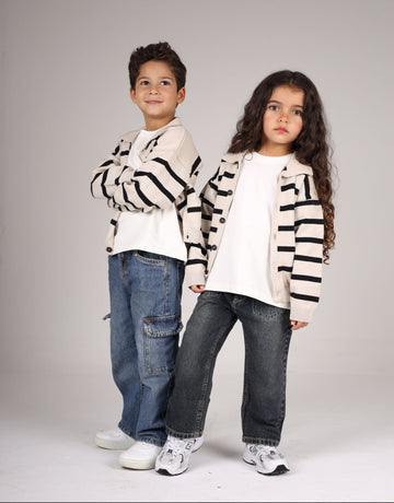Two children wearing matching striped sweaters and jeans on a plain background