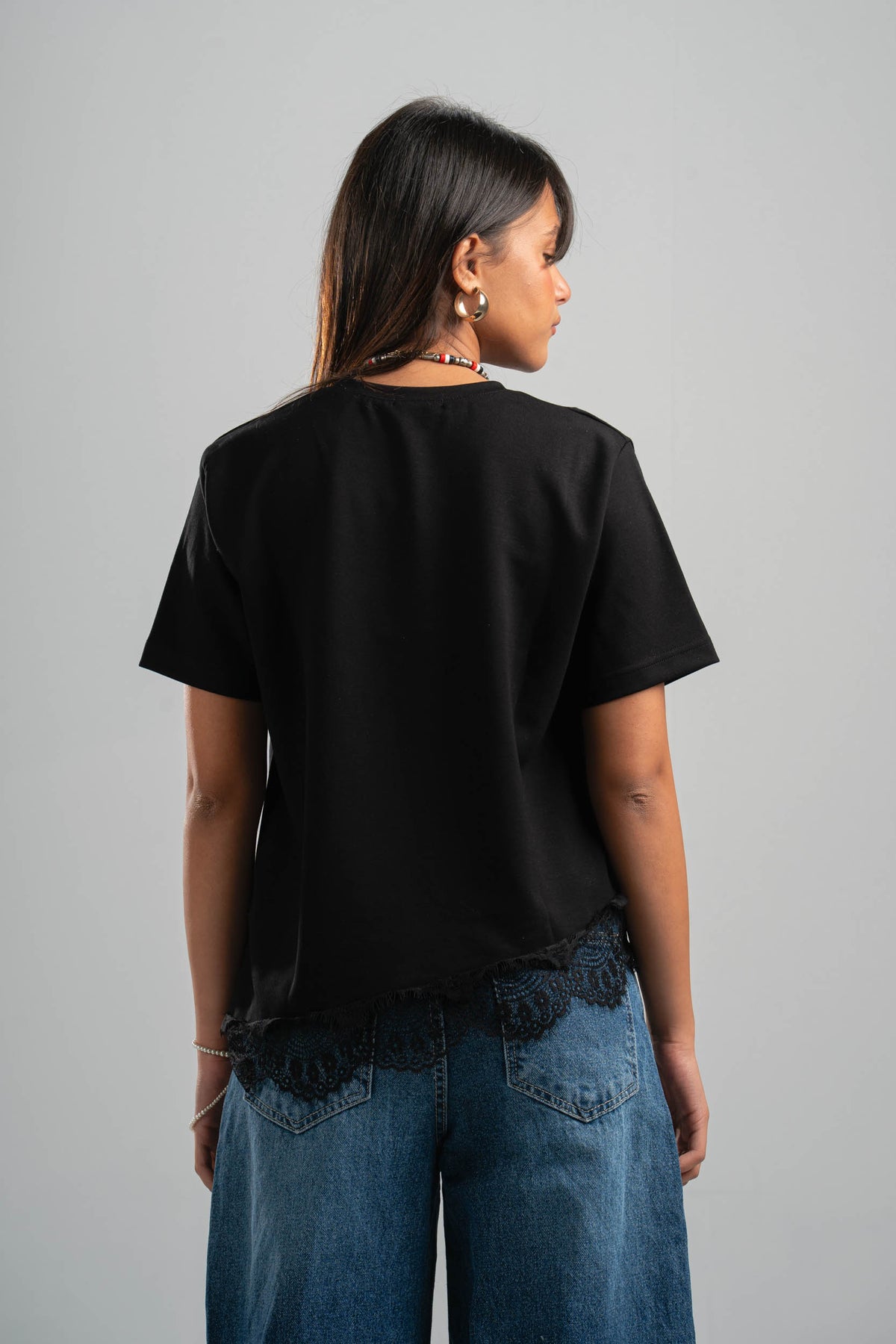 Person wearing a black oversized t-shirt and blue jeans on a gray background