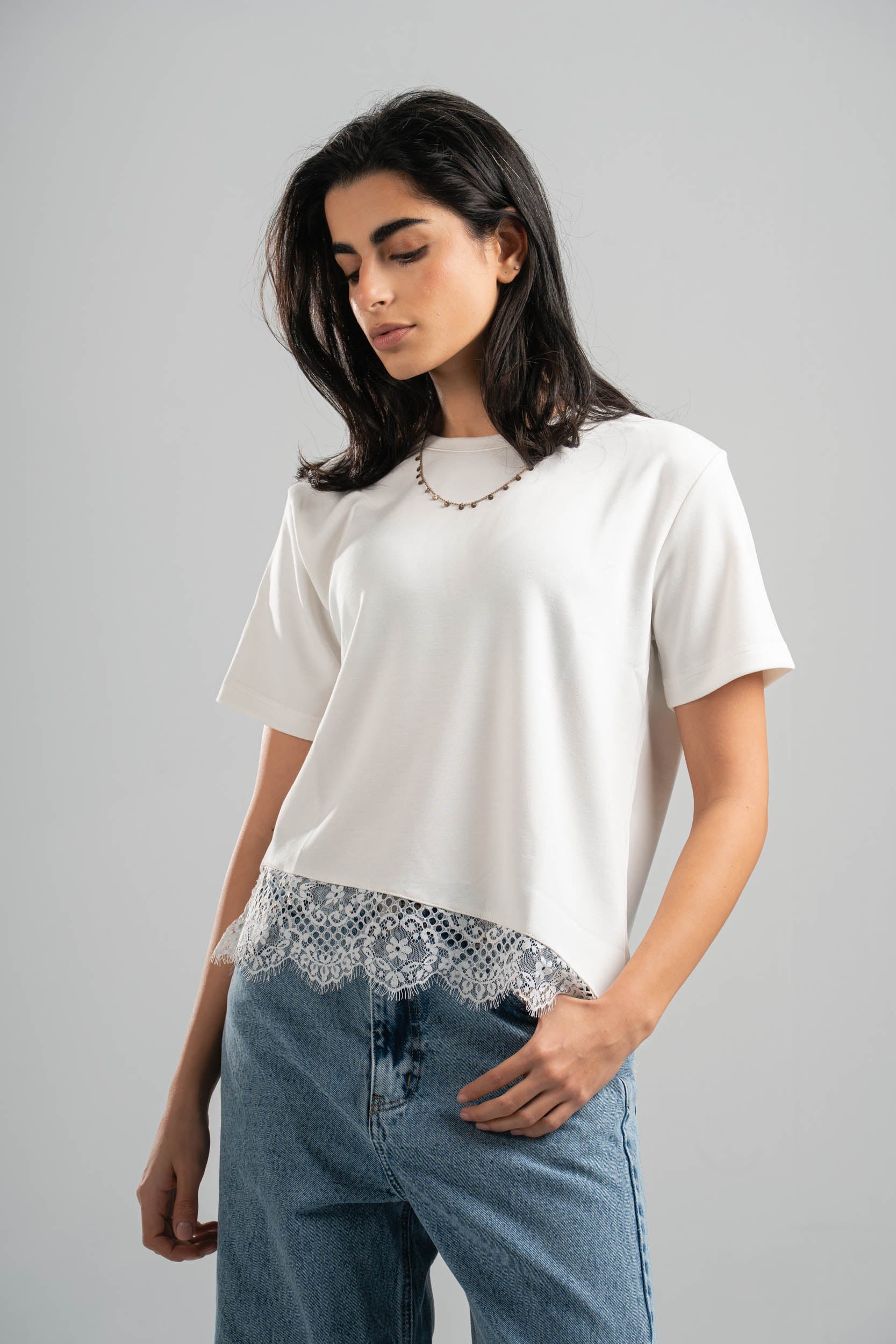 Woman wearing a white t-shirt with lace detailing and blue jeans on a gray background