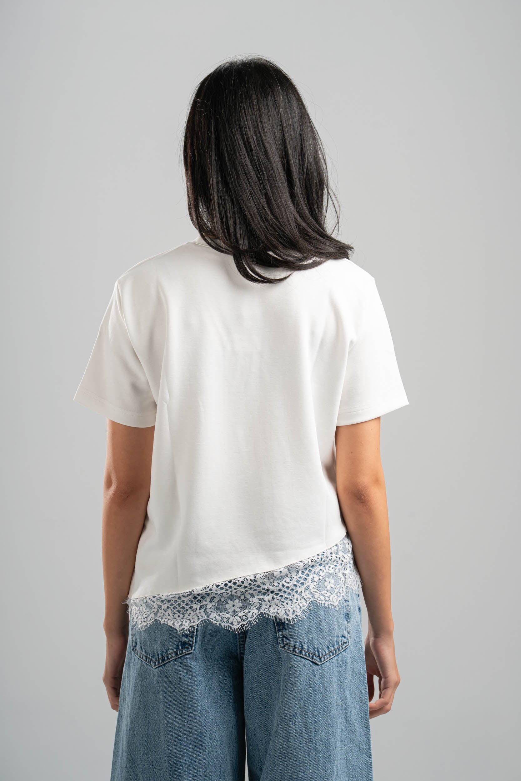 Person wearing a white t-shirt and blue jeans with lace trim, standing against a plain background