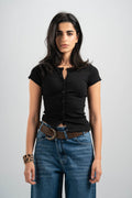 Woman wearing a black top and blue jeans with a belt on a plain background