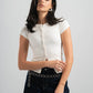 Woman wearing a white blouse and dark jeans with a chain belt against a plain background