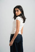 Woman wearing a white top and dark jeans on a plain background