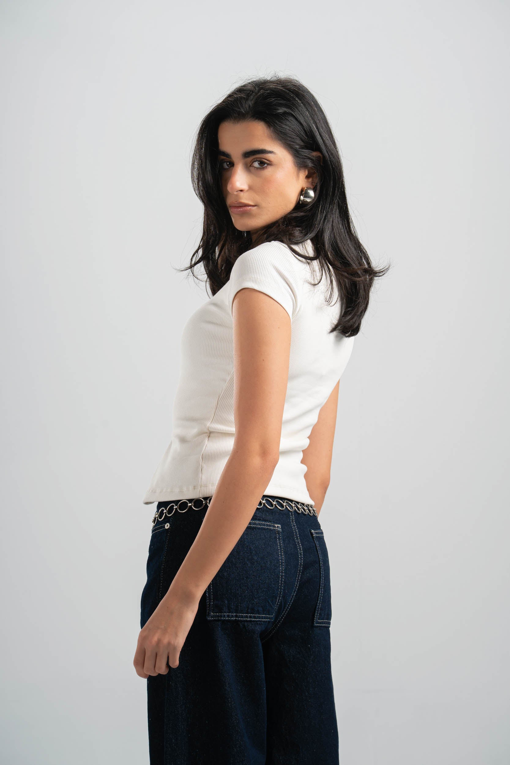 Woman wearing a white top and dark jeans on a plain background