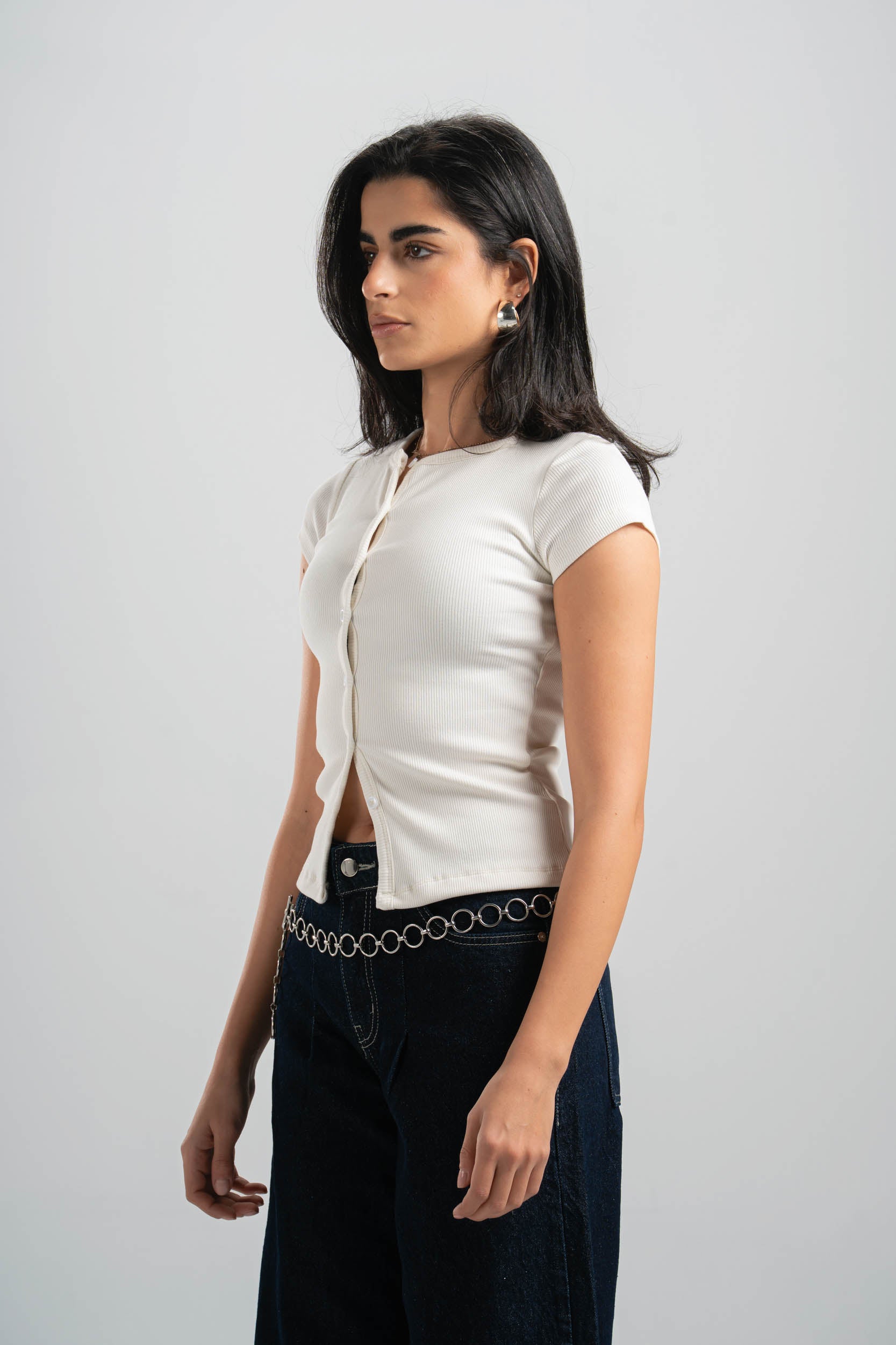 Woman wearing a white blouse with a black belt against a plain background