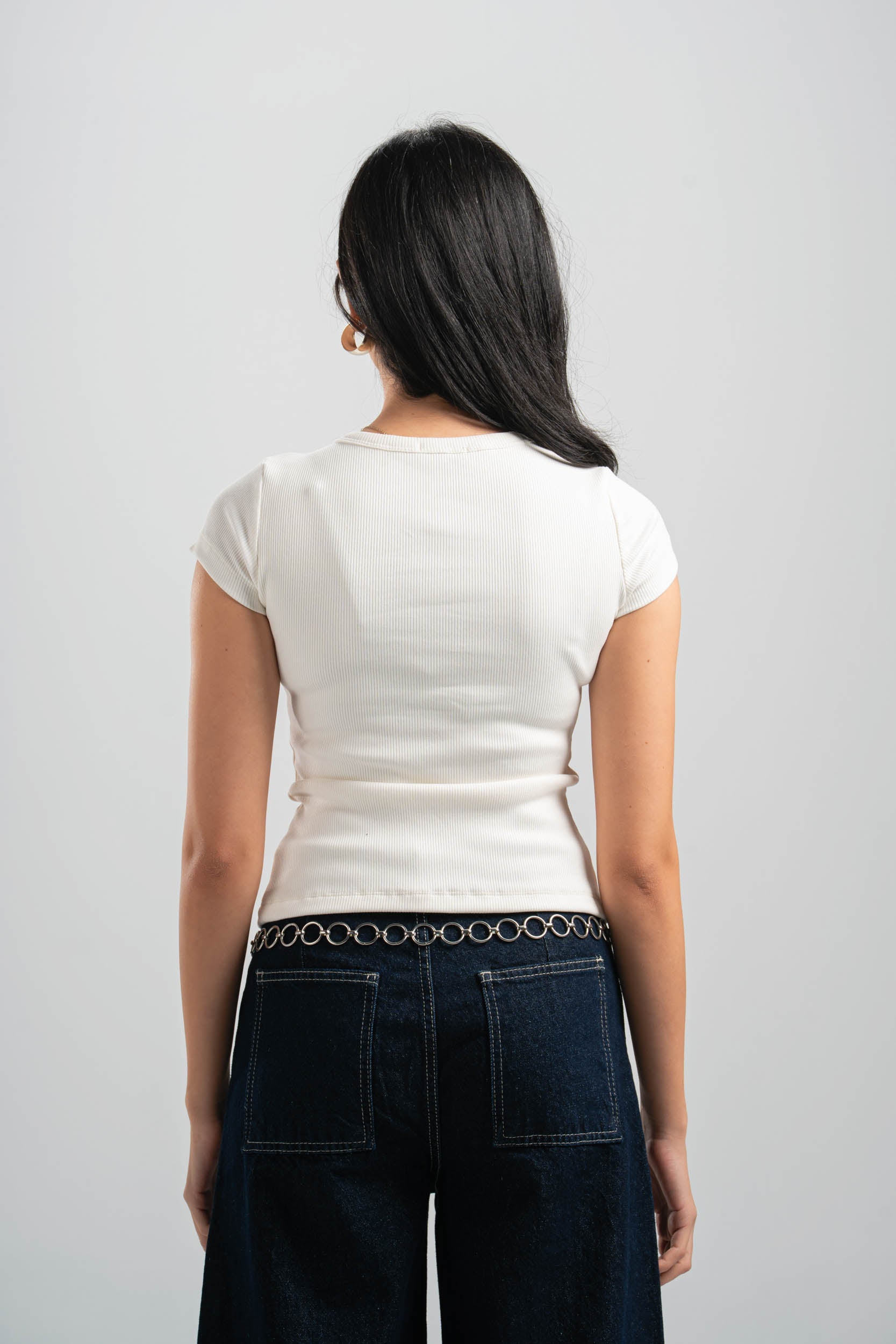 Person wearing a white t-shirt and dark jeans on a plain background