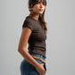 Woman wearing a brown shirt and blue jeans against a gray background